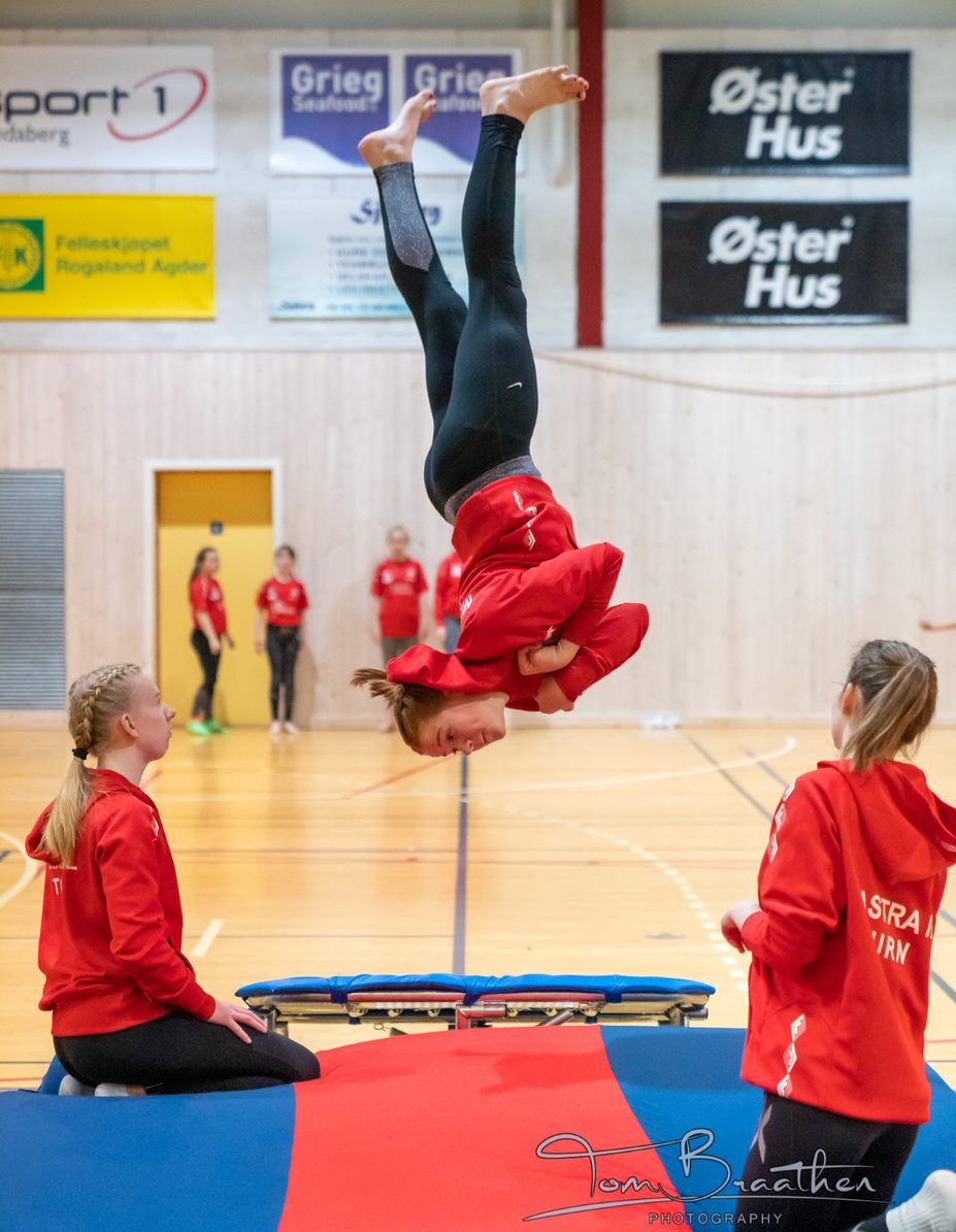 Turnjente i rødskjorte hopper og to andre jenter som sitter